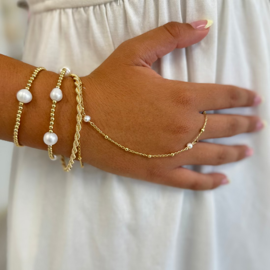 Hand wearing gold bracelets with pearls on a plain background