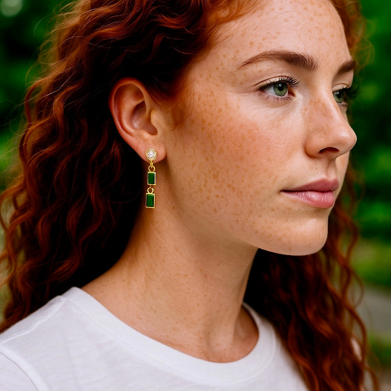 Close-up of a woman wearing gold and green earrings with a blurred green background